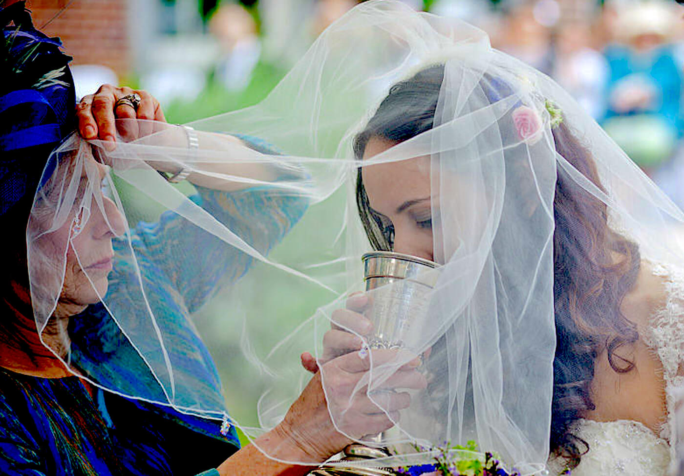 Mother of the bride passing a cup of wine to her daughter during a Jewish wedding iled by a rabbi in Europe.